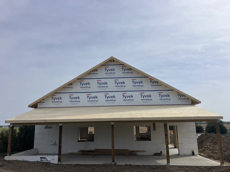 New home with a framed wraparound porch roof and house wrap on the gable