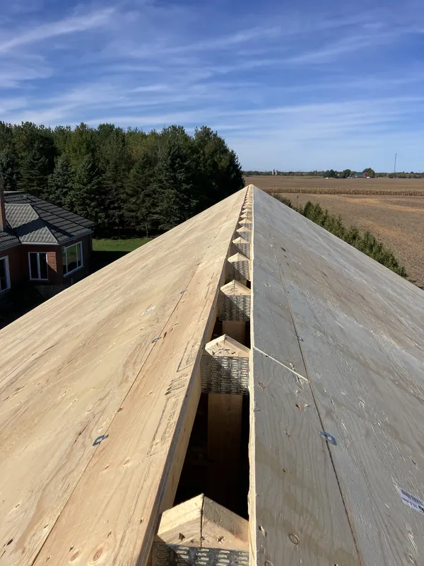 Roof sheathing along the ridge of a new home, with farm fields beyond